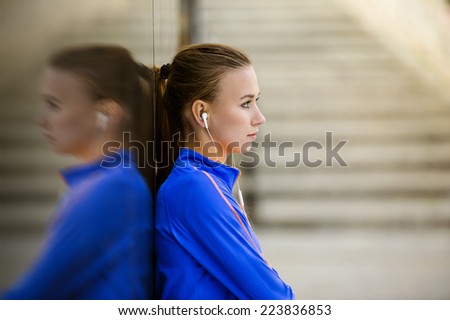 Young female runner is having break and listening to music during the run in city center