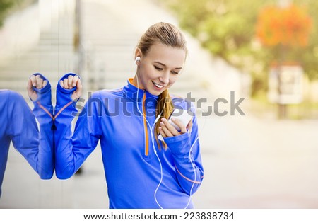 Young female runner is having break and listening to music during the run in city center