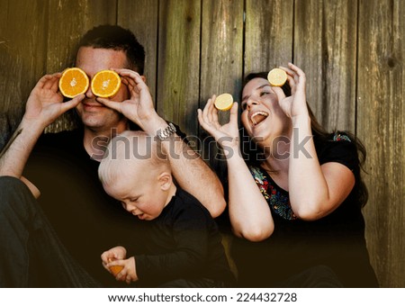 Happy family with little boy sitting by the wooden fence and having fun with oranges