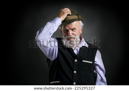 Portrait of old bearded bavarian man in traditional felt hat, posing in studio on black background