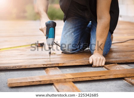 Handyman installing wooden flooring in patio, working with drilling machine
