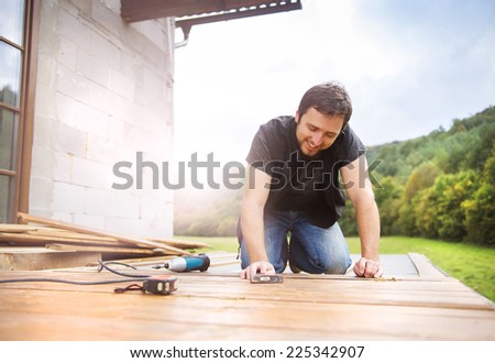 Smiling handyman installing wooden flooring in patio, working with hammer