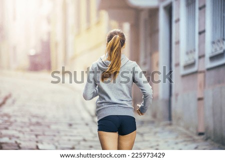 Young female runner is jogging on tiled pavement old city on center. Healthy lifestyle.