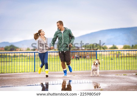 Young couple in colorful wellies walk beagle dog in rain.