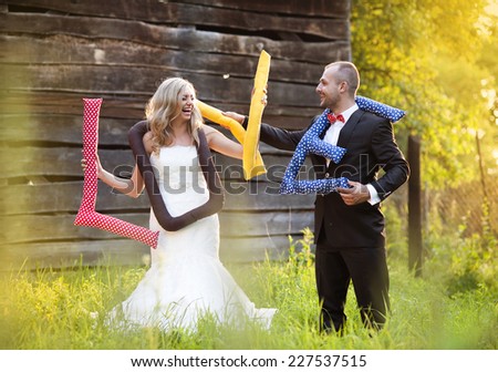 Happy bride and groom on their wedding day having fun with love cushions outside in the garden