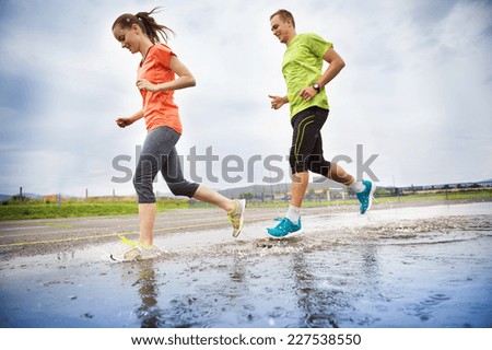 Young couple running on asphalt in rainy weather splashing in puddles.