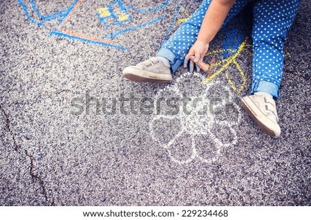 Close up of little girl in canvas shoes drawing with chalks on the sidewalk