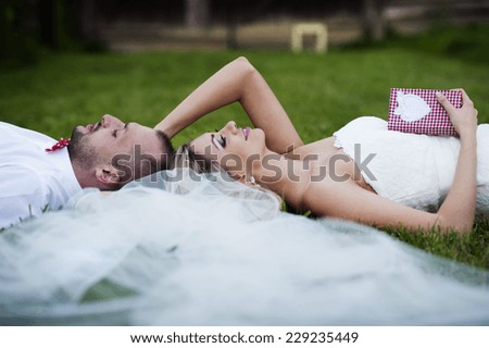Happy bride and groom enjoying their wedding day in green nature, lying on grass