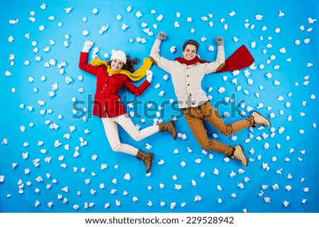 Happy young couplein winter clothes having fun against the blue background with snowflakes