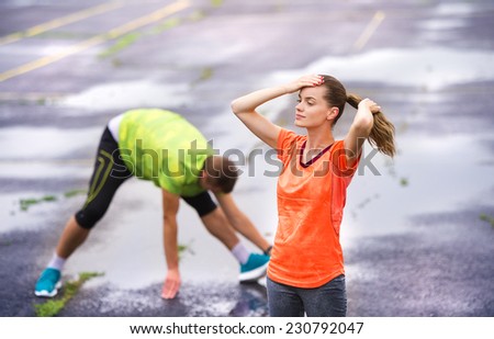 Young couple stretching after the run on asphalt in rainy weather