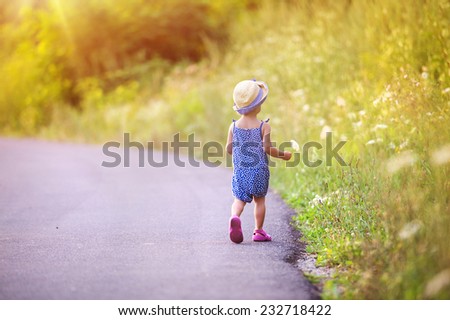 Little child walks on the road in green countryside