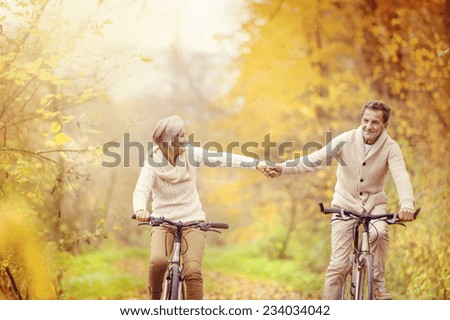 Active seniors riding bike in autumn nature. They relax outdoor.