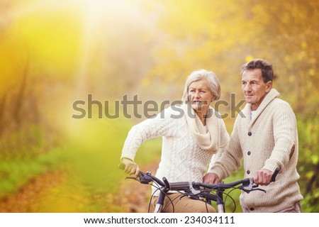 Active seniors riding bike in autumn nature. They relax outdoor.
