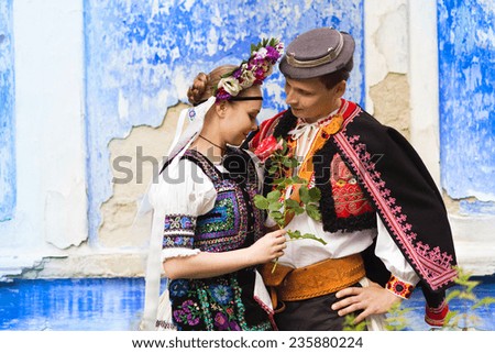 Love couple standing by the blue wall wearing traditional Eastern Europe folk costumes.
