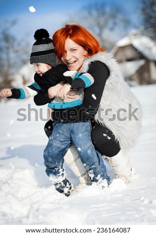 Happy mother with child having fun outside in snow