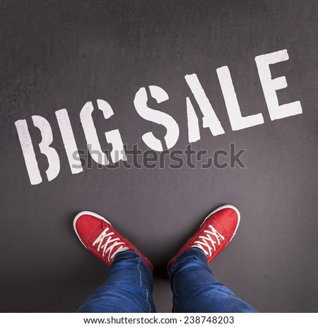 Sale concept with red sneakers and white paint text on black floor