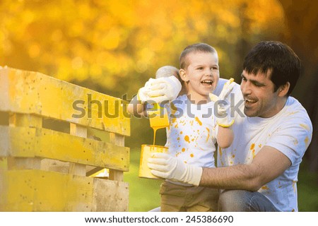 Cute little boy and his father painting wooden fence together on sunny day in nature