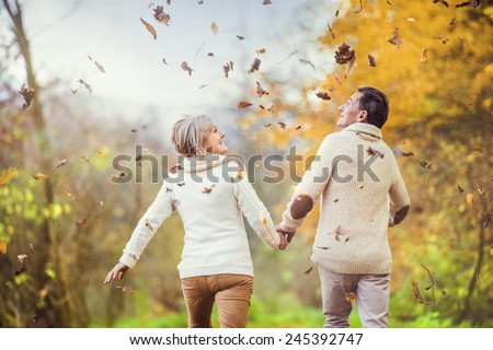 Active seniors having fun and playing with the leaves in autumn forest