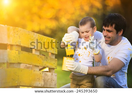 Cute little boy and his father painting wooden fence together on sunny day in nature