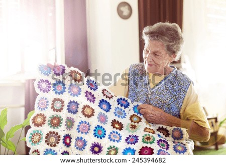 Old woman is knitting a blanket inside in her living room