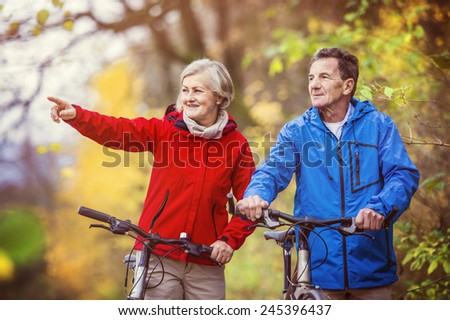 Active seniors having walk with bike in autumn nature. They having romantic time outdoor.