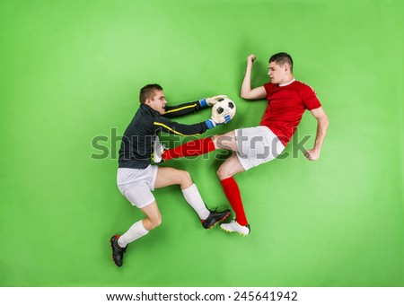 Goalkeeper catching a ball that football player kicks. Studio shot on a green background.
