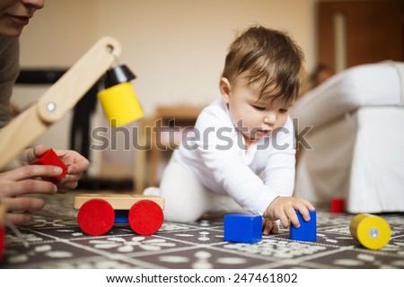Cute little baby girl playing with her mother on a carpet in a living room.