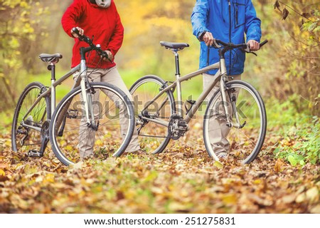 Unrecognizable active seniors having walk with bike in autumn nature. They having romantic time outdoor.
