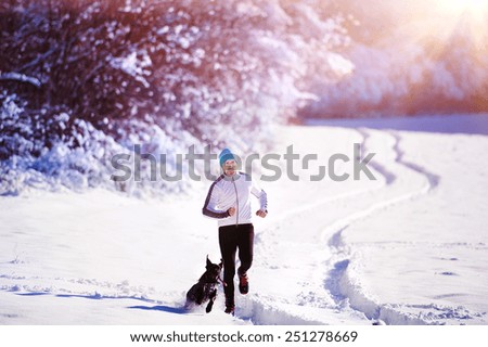 Young sportsman jogging with dog outside in sunny winter park