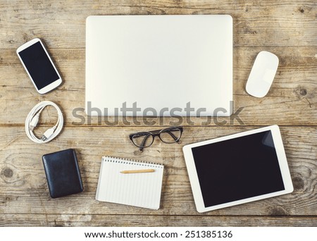 Mix of office supplies and gadgets on a wooden desk background. View from above.