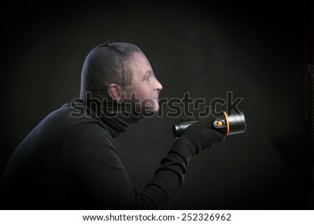 Thief in action with balaclava on his face, dressed in black. Studio shot on black background.