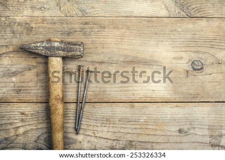Desk of a carpenter with a hammer and two nails. Studio shot on a wooden background.