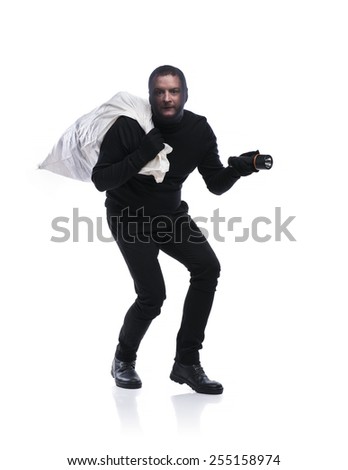 Thief in action carrying a big bag with balaclava on his face, dressed in black. Studio shot on white background.