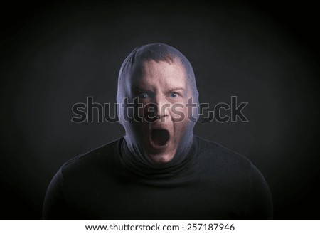Thief in action with balaclava on his face, dressed in black. Studio shot on black background.