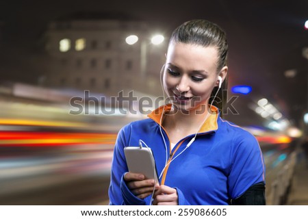 Young woman jogging at night in the city while listening music