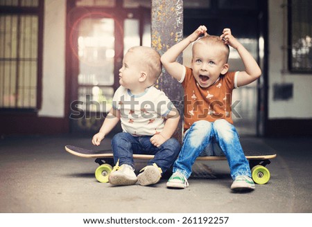 Cute little boys sitting on a skateboard on their walk in the city