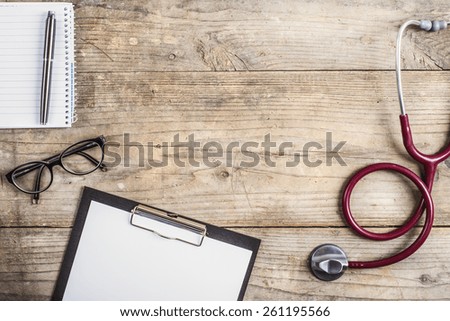 Workplace of a doctor. Stethoscope, clip board, glasses and other things on wooden desk background.