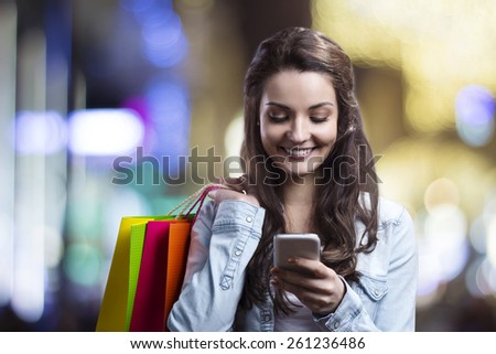Smiling girl with shopping bags and her smart phone in a mall