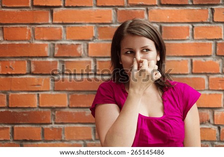 Beautiful young woman making funny faces on a brick wall background