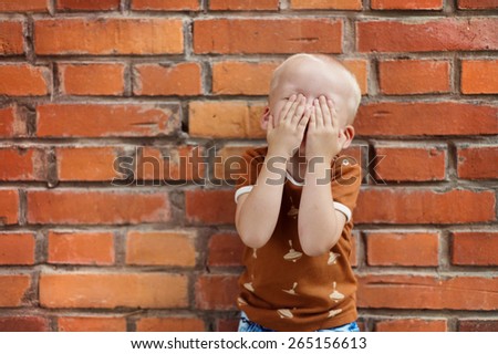 Cute little boy making funny faces on a brick wall background
