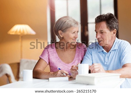 Happy senior couple sitting at the table making plans and drinking coffee in their living room.