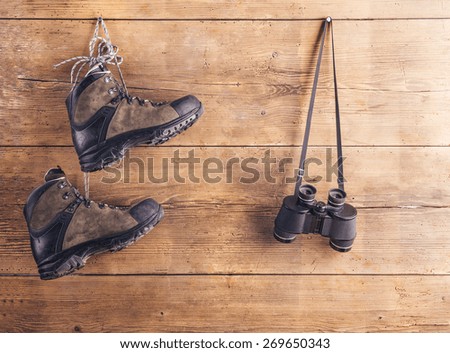 Hiking shoes and binoculars hang on a wooden fence background