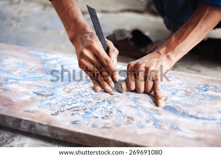 Vietnamese craftsman carving out and painting a floral pattern on a wooden board