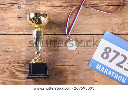 Cup, medal and race number on a wooden floor background