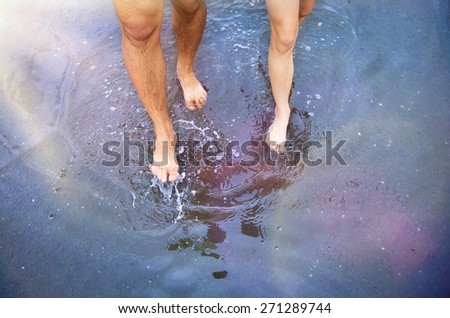 Unrecognizable woman and man walking barefoot through a puddle