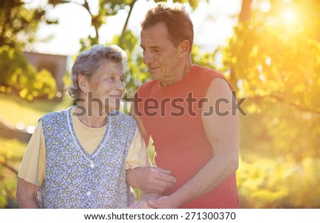 Senior woman in apron with her elderly son in her garden.