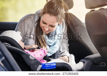 Mother in a car, having her little baby girl in a child seat