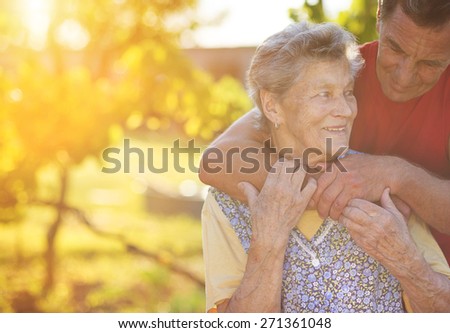 Senior woman in apron with her elderly son in her garden.