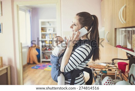 Young mother talking on a phone having her baby in a carrier