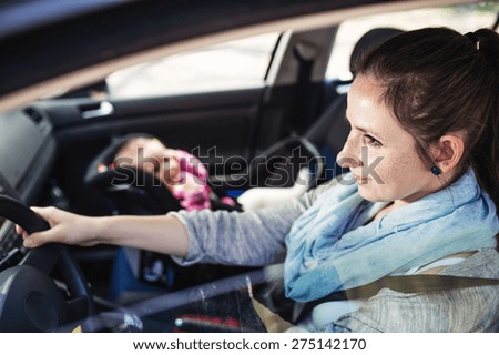 Mother driving a car, having her little baby girl in a child seat